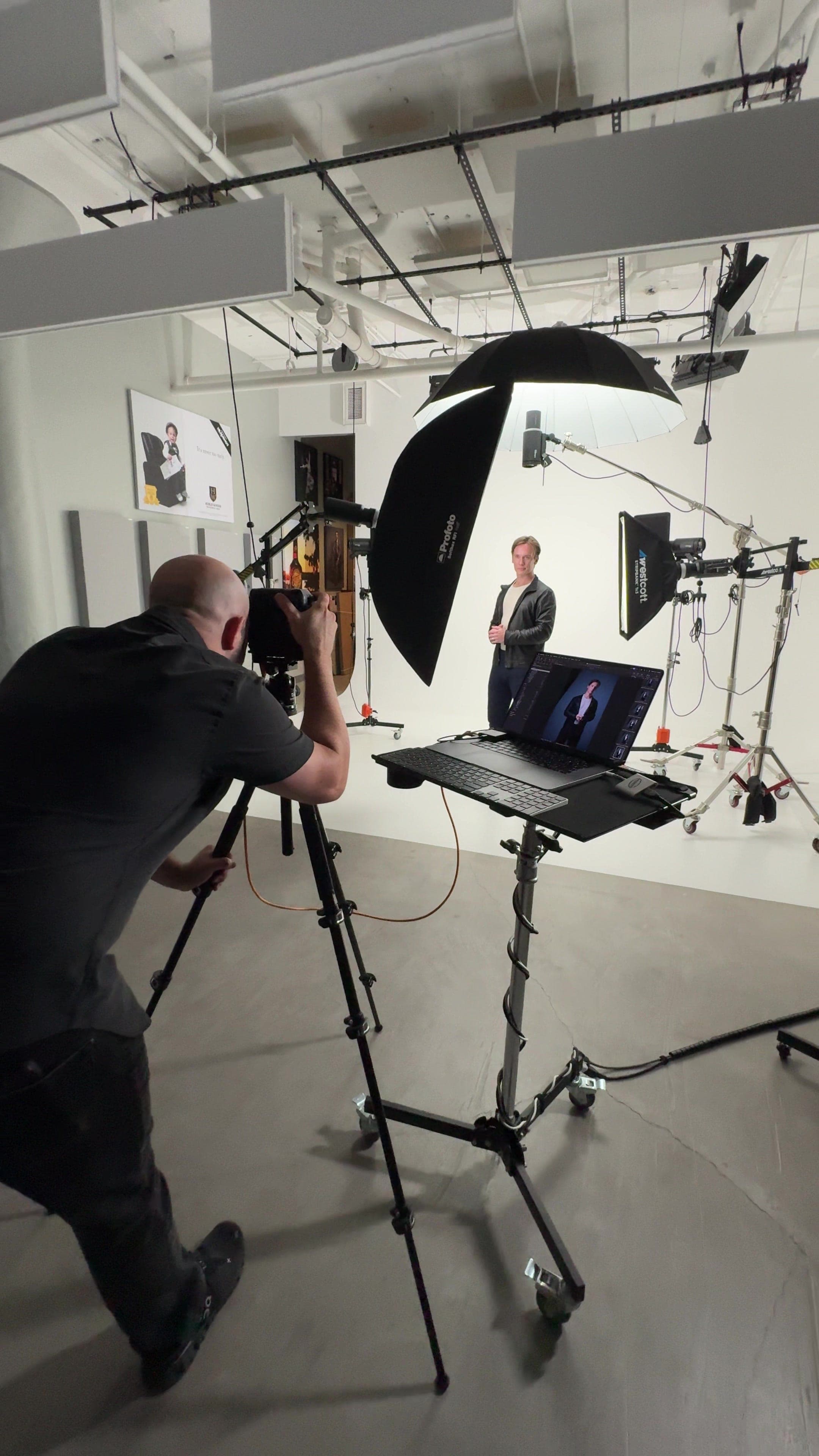 Garrett Shearman standing for a portrait on a white studio set, a photographer and tethered laptop in the foreground